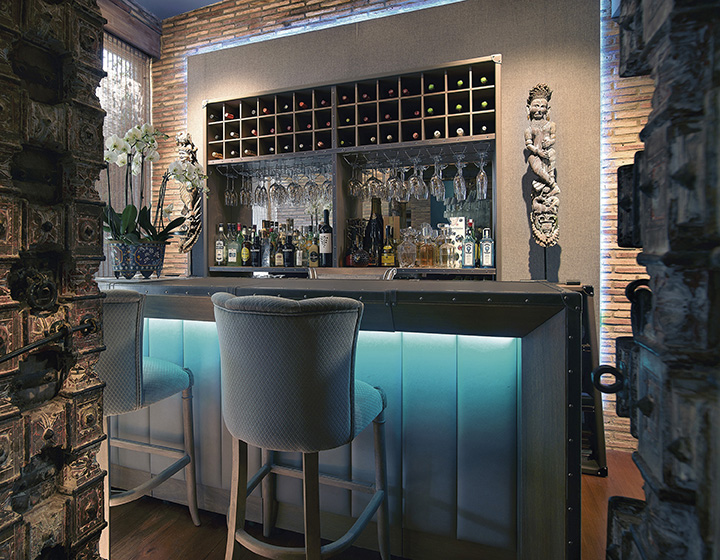 Zona de bar en casa de estilo clásico compuesta por una barra, taburetes altos y un amplio mueble botellero.
