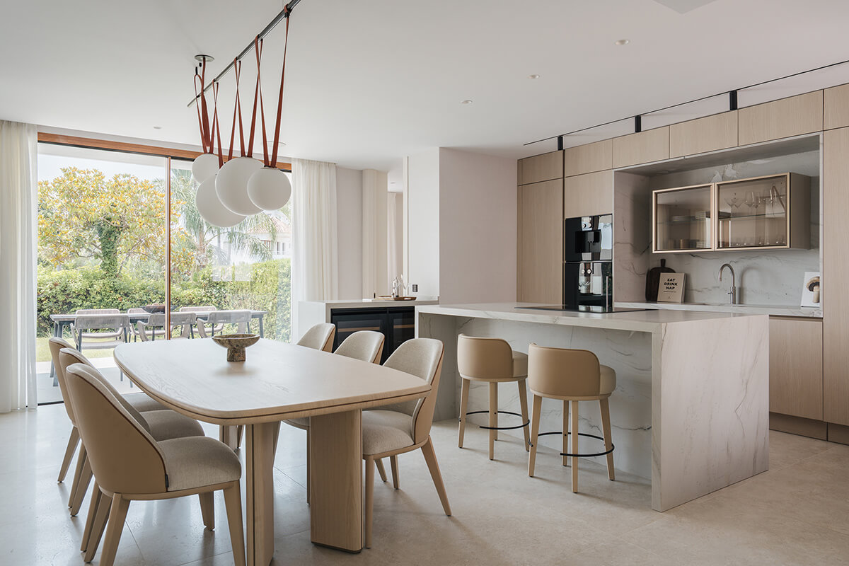 Comedor de diseño con mesa Decorte de fresno, sillas Atlas y lámparas colgantes junto a grandes ventanales en Marbella